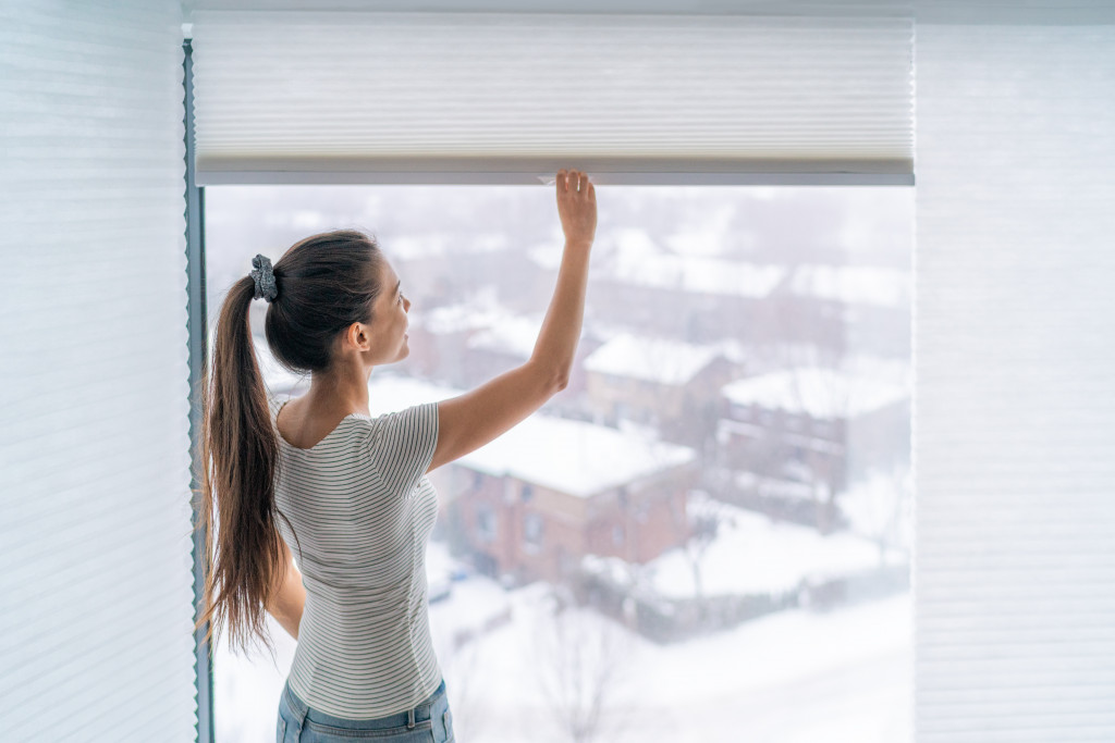 A woman lifting the blinds to see a snow-covered town